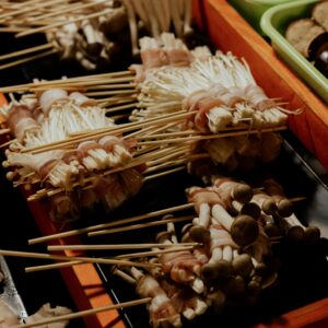 A vibrant display of skewered mushrooms wrapped in bacon at a street food stall, showcasing diverse Asian cuisine.
