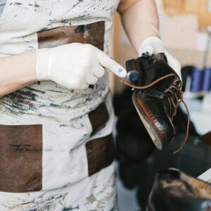 A craftsman polishing black leather shoes with gloves in a workshop setting.