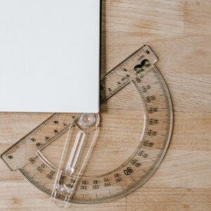Composition of protractor under white sheet of paper on wooden table in school
