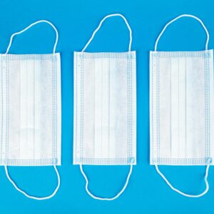 Three white medical masks arranged on a vibrant blue background, flat lay view.