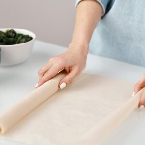 Person rolling dough for baking with ingredients on a kitchen counter.