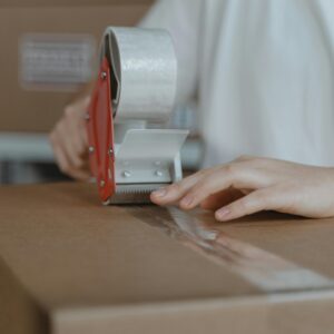 A person sealing a cardboard box with a tape dispenser in an indoor setting.