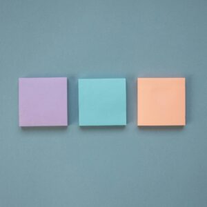 Three pastel-colored Post-It Notes arranged in a neat row on a blue backdrop.