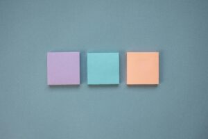 Three pastel-colored Post-It Notes arranged in a neat row on a blue backdrop.