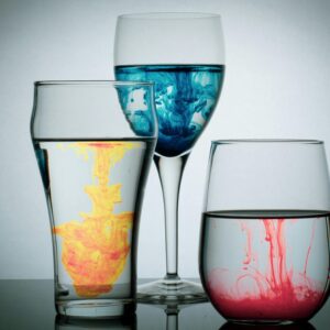 Vibrant acrylic paint swirling in glasses creating mesmerizing patterns against a neutral backdrop.