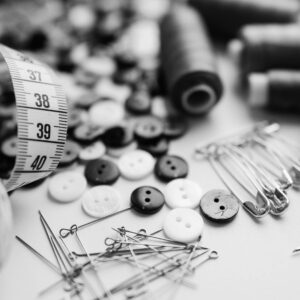 Black and white sewing materials including buttons, needles, and thread spools on a white surface.