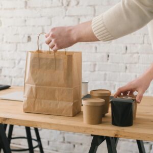 Hand arranging takeaway food packaging on a wooden table with brick wall background.