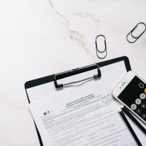 A flat lay of W-7 IRS form, smartphone calculator, and paper clips for tax preparation.