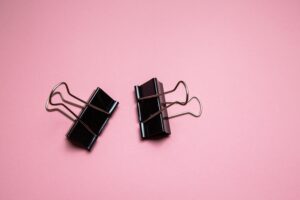 Top view pair of black metal paper binder clips placed on pink table in studio