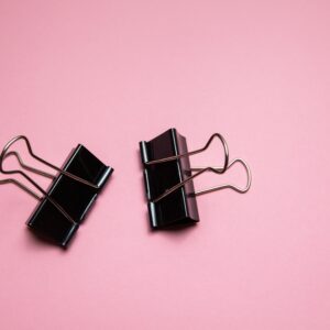 Top view pair of black metal paper binder clips placed on pink table in studio