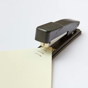 A close-up image of a black stapler fastening sheets of paper, ideal for office themes.