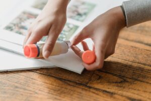 Crop anonymous person gluing set of photos to poster on wooden surface in daylight