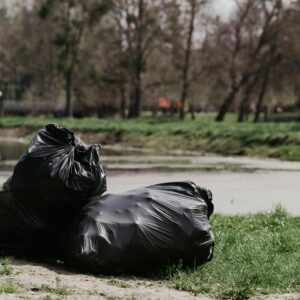 Two black garbage bags on grass by a riverside in a park.