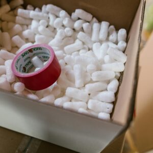 Close-up of a cardboard box filled with packing peanuts and red tape.