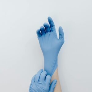 Close-up of hands putting on blue medical gloves against a white backdrop.