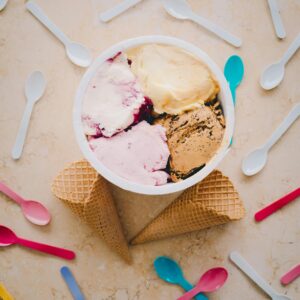 A vibrant flat lay of ice cream pints with cones and colorful plastic spoons.