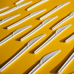 White plastic knives arranged on a vibrant yellow surface, emphasizing pollution and waste concepts.