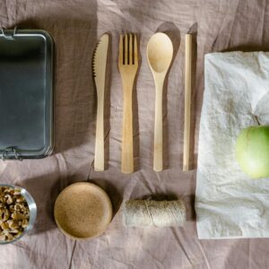 A flat lay of eco-friendly lunch items including wooden cutlery and a green apple.