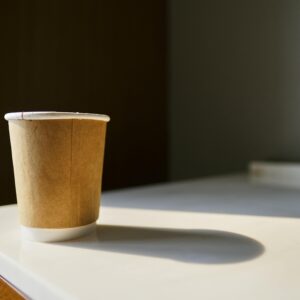 Close-up of a brown paper cup casting a shadow on a sunlit table, perfect for copy space needs.