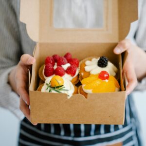 Close-up of a woman holding a box filled with assorted fresh fruit cupcakes, perfect for dessert.