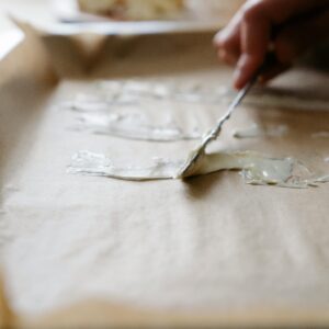 Close-up of hand spreading butter on baking tray lined with parchment paper, preparing for baking.