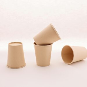 Four brown disposable paper cups arranged on a white surface. Ideal for eco-friendly concepts.