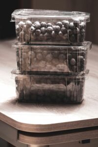 Stacked plastic containers filled with fresh blueberries on a wooden table in soft lighting.