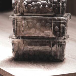 Stacked plastic containers filled with fresh blueberries on a wooden table in soft lighting.
