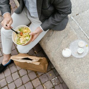 A person enjoys a fresh vegetable salad seated outdoors, capturing a casual urban lunch moment.