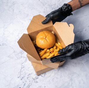 PP Takeaway Boxes Delicious burger and seasoned fries in a cardboard takeout box, held by gloved hands.