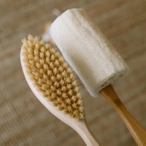 A detailed close-up of a natural wooden body brush and loofah on a textured surface.