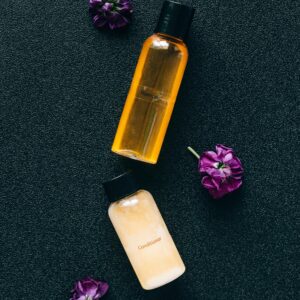 Top view of cosmetic bottles with purple flowers on a textured surface, creating a stylish composition.