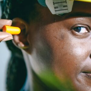 A close-up image of a woman inserting an earplug, wearing safety gear.
