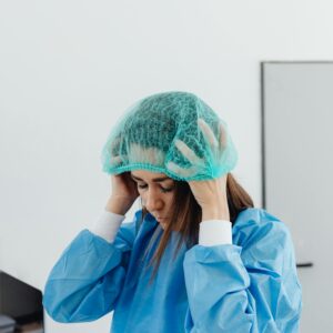 Female healthcare worker in lab adjusting protective cap and gown, focused and professional.