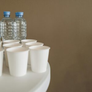 Close-up of disposable cups and bottled water with copyspace on a white table.