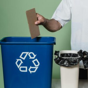 A person placing cardboard into a blue recycling bin, promoting eco-friendly practices indoors.