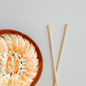 Top view of a plate of gyoza with chopsticks on a minimalist background.