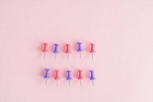 Pink and purple push pins neatly arranged on a soft pink surface.