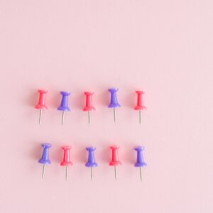 Pink and purple push pins neatly arranged on a soft pink surface.