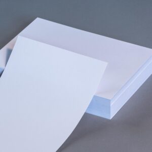 A high-quality image showing blank white paper sheets stacked on a neutral gray surface.