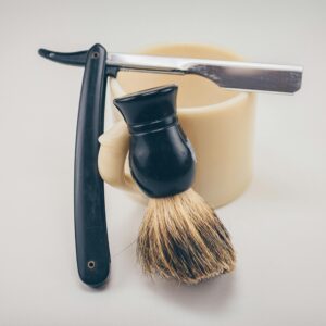 Still life of barber tools including a straight razor, shaving brush, and mug.